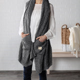 Demdaco Giving Shawl in charcoal (27″×70″), buttery‑soft fabric with two pockets—giftable hug, available at Be Charmed.