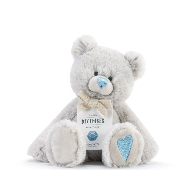 A plush teddy bear with a birthstone theme, featuring a ribbon around its neck that indicates the month of December.  Available at Be Charmed