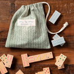 Demdaco Dots to Dots Domino Set, 28 wooden tiles with colored dots in green‑cream herringbone cotton drawstring bag—available at Be Charmed.