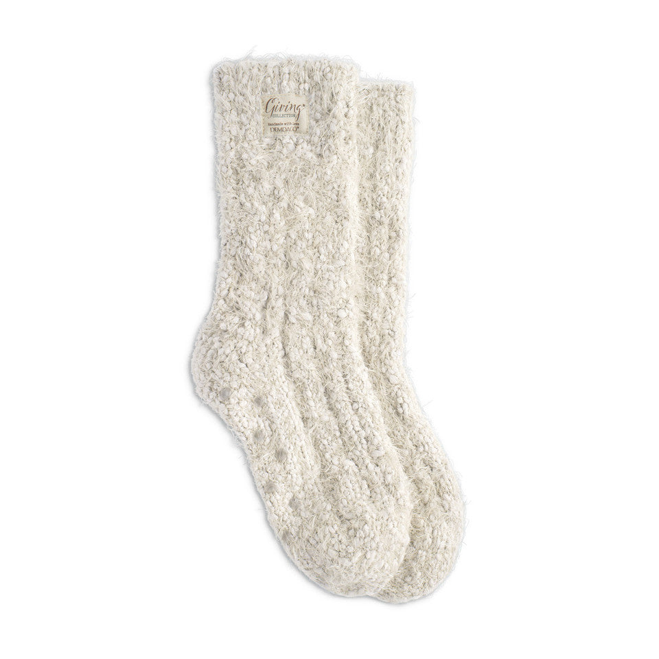 A pair of cream-colored fuzzy giving socks with grippers, displayed against a white background. Available at Be Charmed