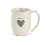 A beige ceramic mug with a heart shape design and the word 'grateful' printed on it. Available at Be Charmed