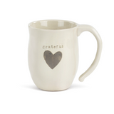 A beige ceramic mug with a heart shape design and the word 'grateful' printed on it. Available at Be Charmed