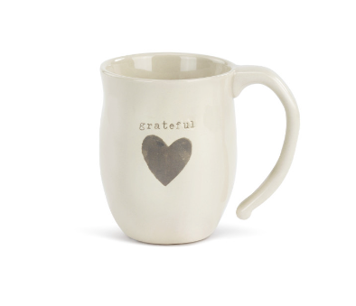 A beige ceramic mug with a heart shape design and the word 'grateful' printed on it. Available at Be Charmed