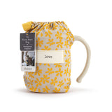 Mug with yellow floral pattern and 'love' tag, branded 'DEVAICO'. Available at Be Charmed