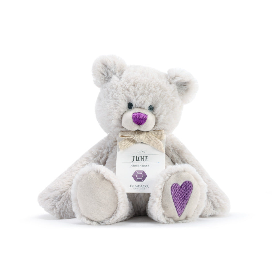 A plush teddy bear with a birthstone theme, featuring a ribbon around its neck that indicates the month of June. Available at Be Charmed