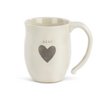 A beige ceramic mug with the word 'kind' and a heart shape on it. Available at Be Charmed