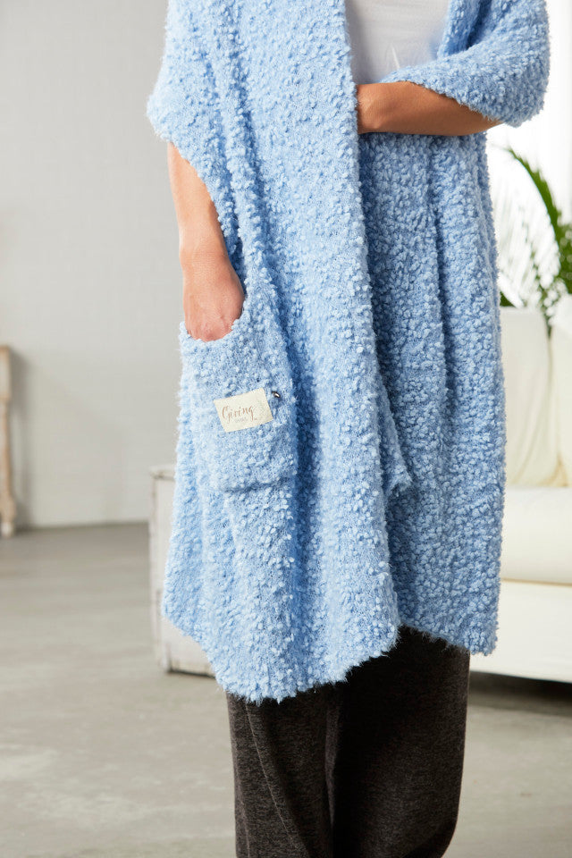 Demdaco Giving Shawl in light blue (27″×70″), buttery‑soft fabric with two pockets—giftable hug, available at Be Charmed.