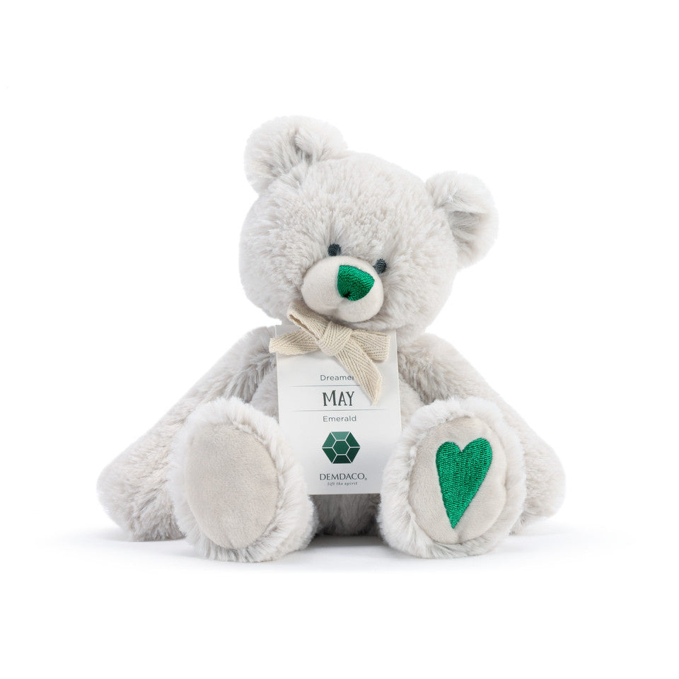 A plush teddy bear with a birthstone theme, featuring a ribbon around its neck that indicates the month of May. Available at Be Charmed