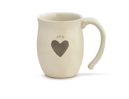 A beige ceramic mug with a heart shape and the word 'mom' printed on the side. Available at Be Charmed