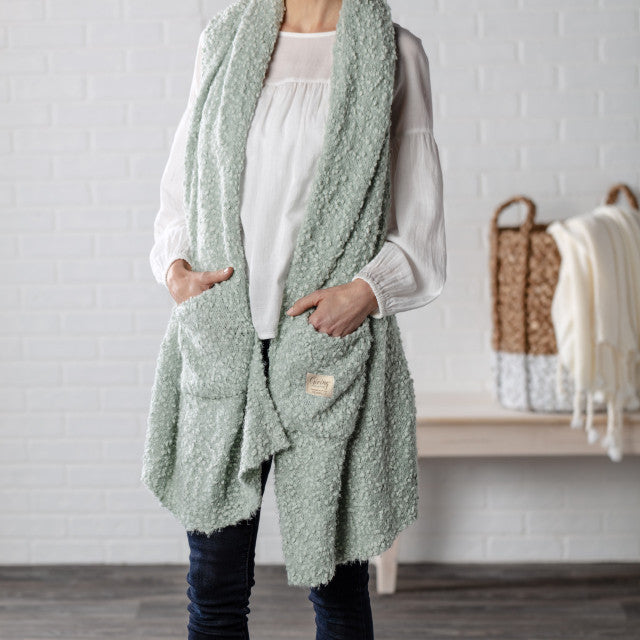 Demdaco Giving Shawl in sage (27″×70″), buttery‑soft fabric with two pockets—giftable hug, available at Be Charmed.