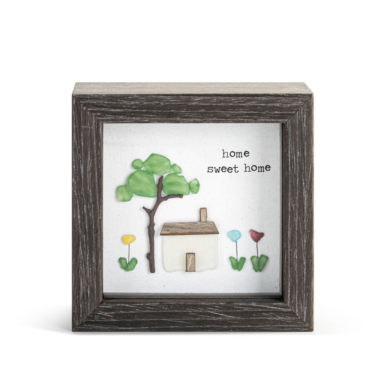 A shadow box with a 'Home Sweet Home' text, featuring a tree and a small house, framed in a brown wooden composite structure. Available at Be Charmed