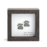 A shadow box with a wooden frame, featuring a silhouette of a pet's paw print on a heart-shaped background, with the text 'Paw Prints on My Heart'. Available at Be Charmed