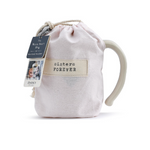 Demdaco "Sisters Forever" Heart Mug pictured in pouch, 16 oz stoneware with hand-thrown feel and heart cutout, microwave & dishwasher safe—available at Be Charmed.