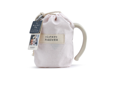 Demdaco "Sisters Forever" Heart Mug pictured in pouch, 16 oz stoneware with hand-thrown feel and heart cutout, microwave & dishwasher safe—available at Be Charmed.