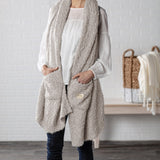 Demdaco Giving Shawl in taupe (27″×70″), buttery‑soft fabric with two pockets—giftable hug, available at Be Charmed.