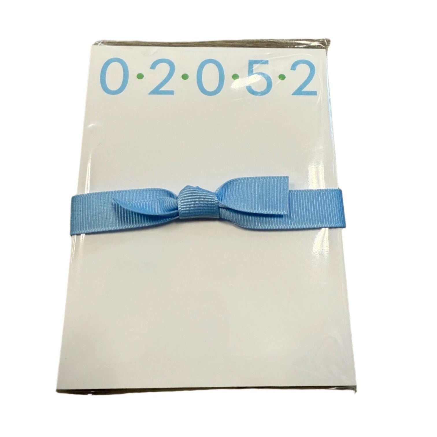 A compact Donovan Designs mini notepad in blue color with a blue ribbon tied on it, featuring the zip code 02052 on the front cover. Available at Be Charmed