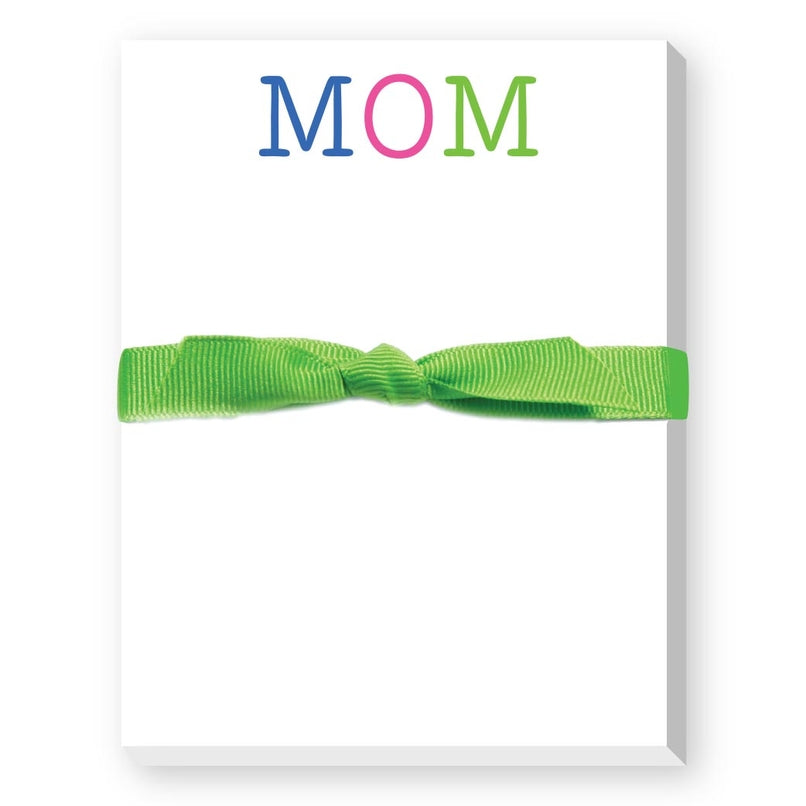 A mini notepad with 'MOM' written on the cover in colorful letters, tied with a green ribbon. Available at Be Charmed