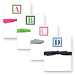 Mini notepads with various initial letters and colored ribbons on top, presented in a square format. Available at Be Charmed