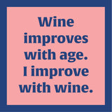 Text 'Wine improves with age. I improve with wine.' on a pink coaster with blue text. Available at Be Charmed