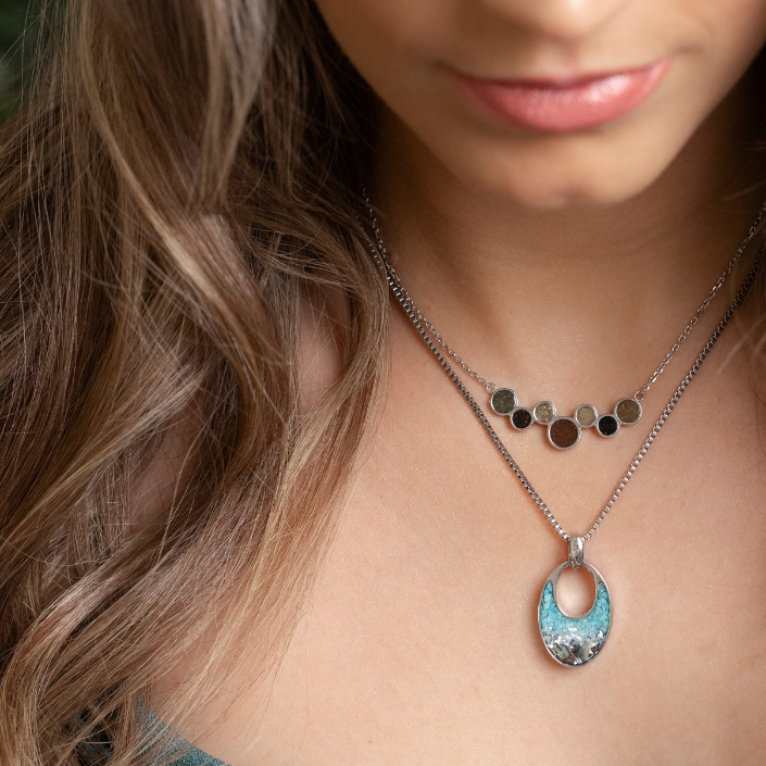 Close-up of a woman wearing a necklace with a blue pendant. Available at Be Charmed