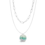 Layered Silver Necklace with a round pendant featuring a wave design on a white background. Available at Be Charmed