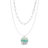 Layered Silver Necklace with a round pendant featuring a wave design on a white background. Available at Be Charmed