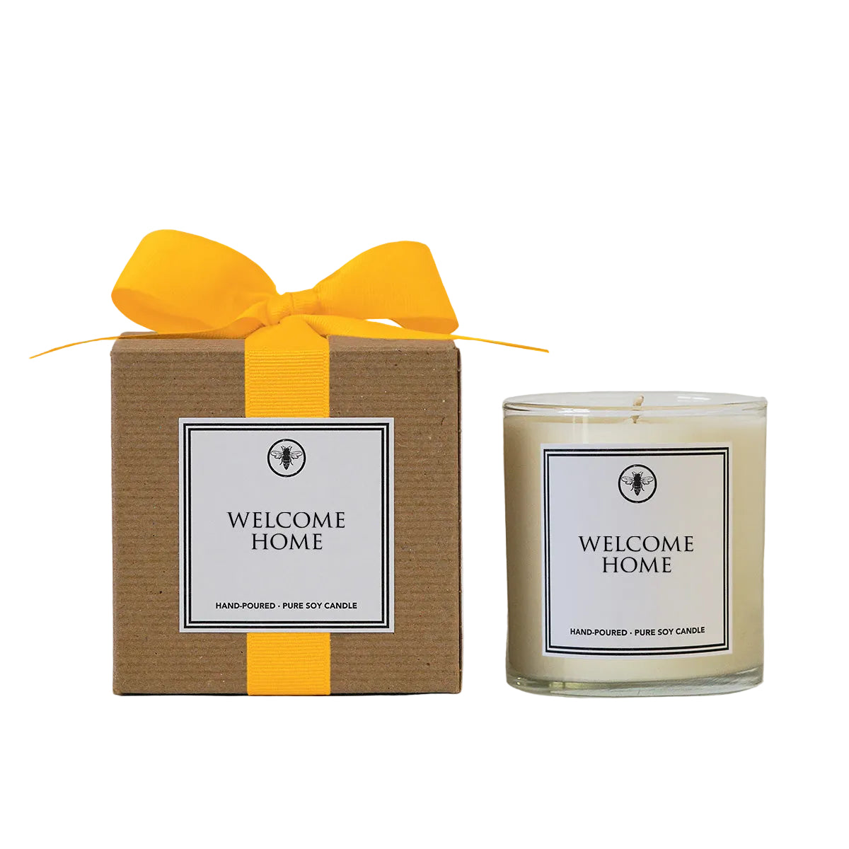 Candle labeled 'Welcome Home' with a matching box and yellow ribbon on a light gray background. Available at Be Charmed