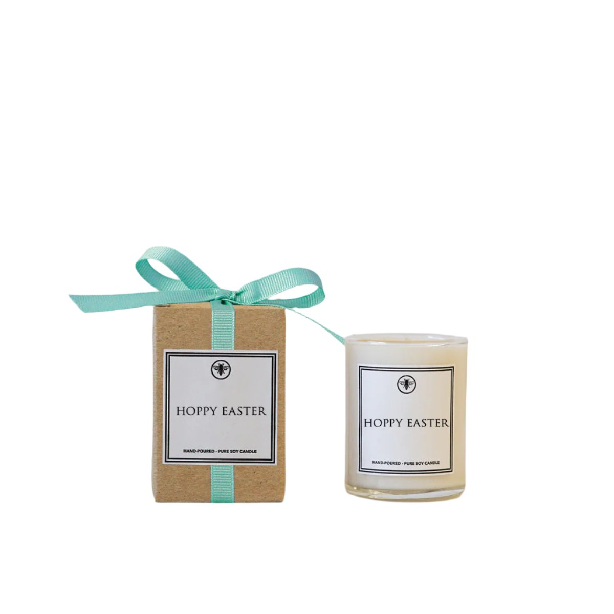A beige candle with a 'Hoppy Easter' label, placed inside a brown paper wrapper with a turquoise ribbon. Available at Be Charmed