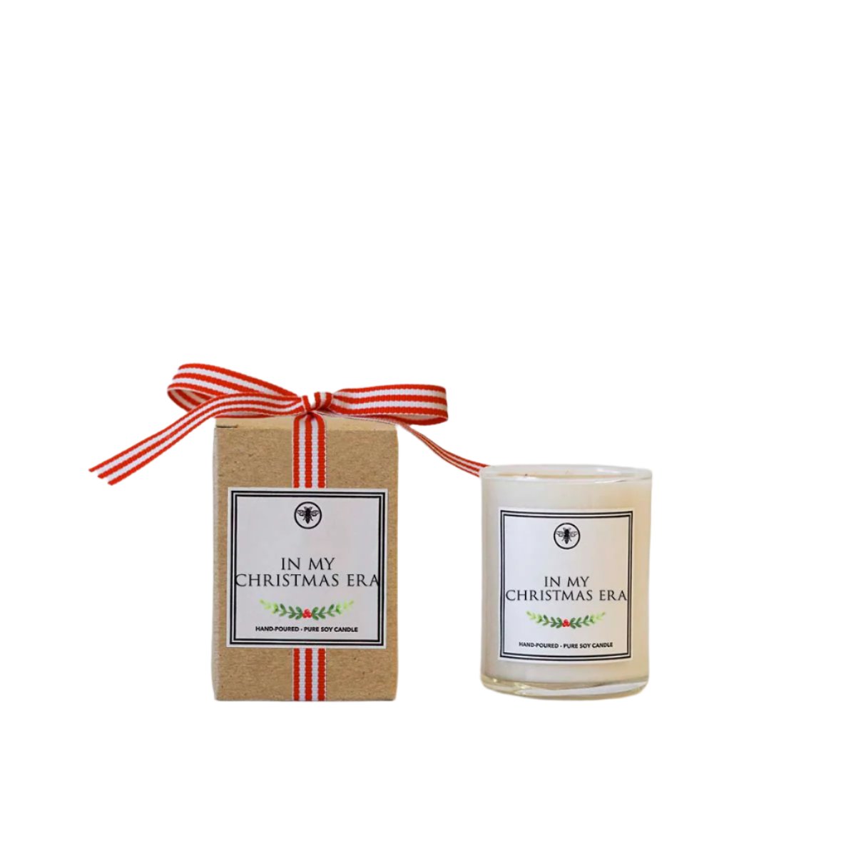 A clear glass candle with a red and white label that reads 'In My Christmas Era' by Ella B, tied with a red ribbon and presented in a beige cardboard box with a grosgrain bow. Available at Be Charmed