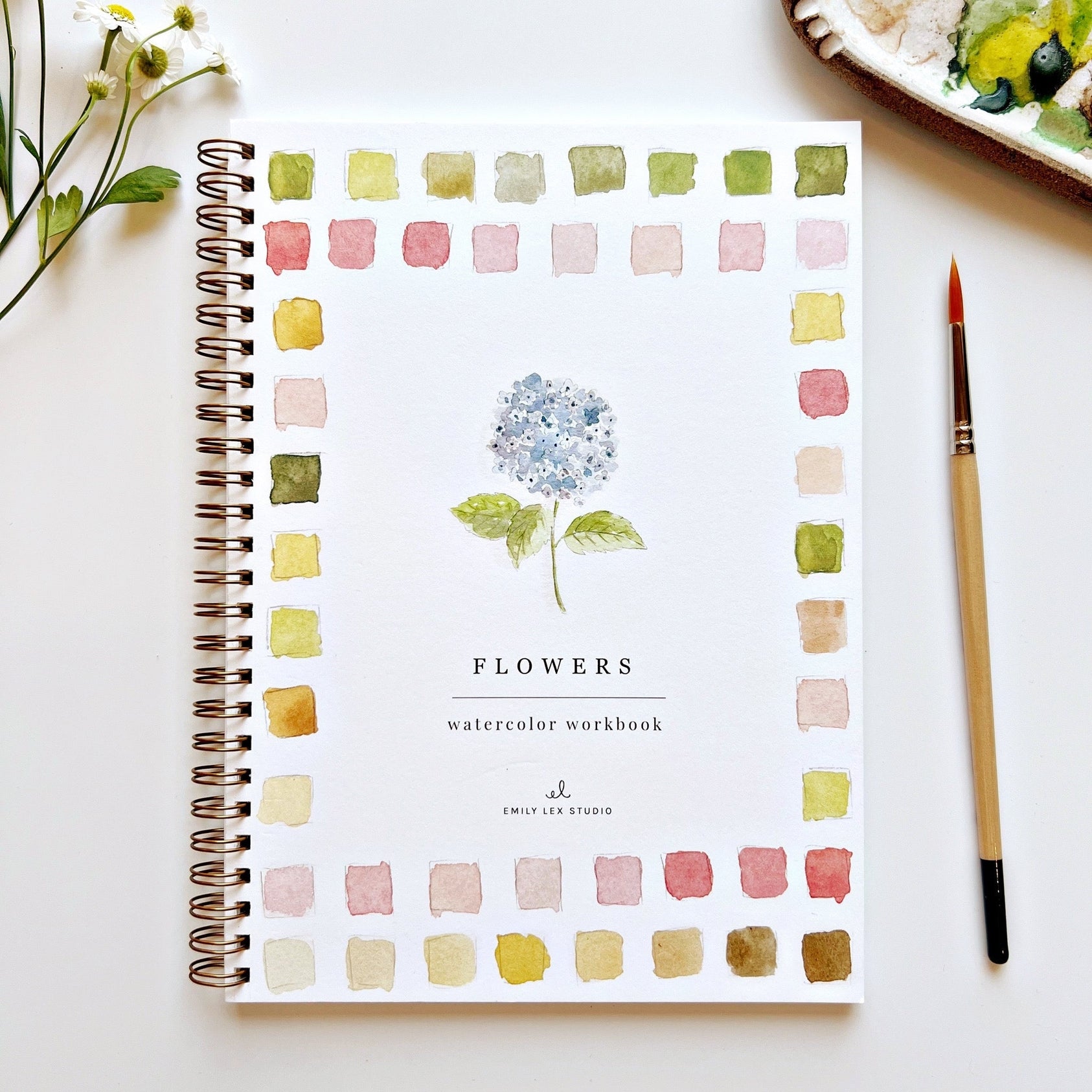 Watercolor workbook titled 'Flowers' by Emily Lex Studio on a white surface with a paintbrush and flowers. Available at Be Charmed