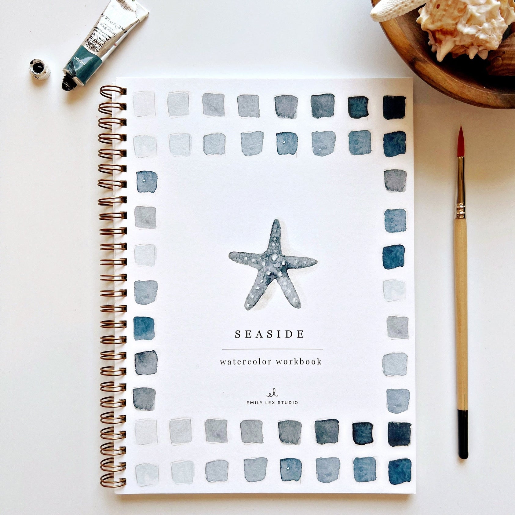 Seaside watercolor workbook with starfish design on a white surface with art supplies. Available at Be Charmed