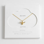 Gold bee necklace on a white card with 'Estella Bartlett' branding. Available at Be Charmed