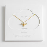 Gold bee necklace on a white card with 'Estella Bartlett' branding. Available at Be Charmed