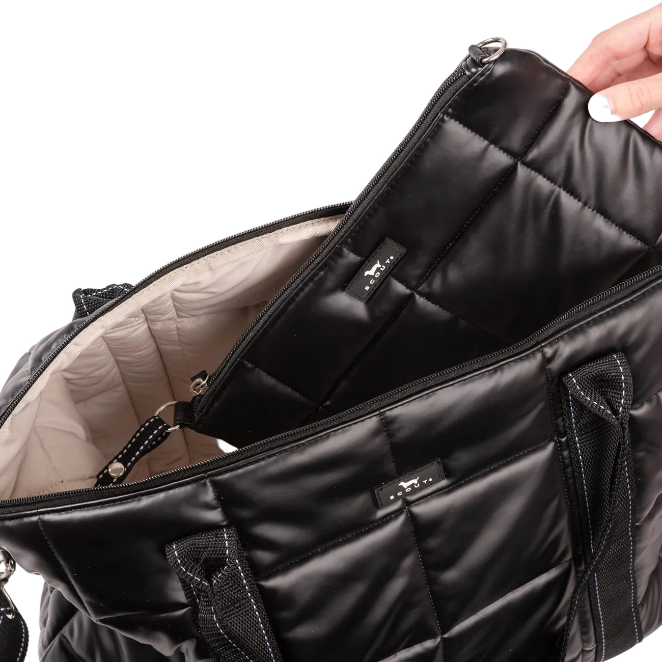 Black quilted Scout bag with a hand opening it on a light white background. Available at Be Charmed