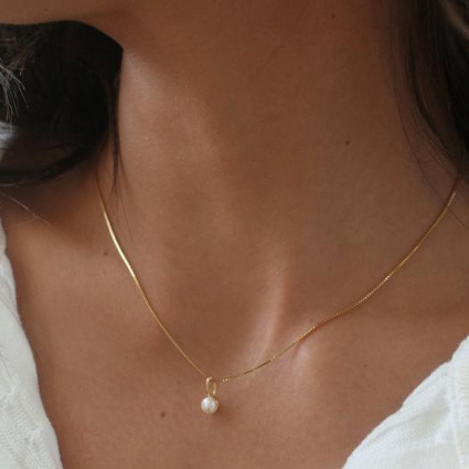 Gold necklace with a pearl pendant on a person wearing a white top. Available at Be Charmed