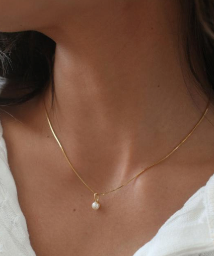 Gold necklace with a pearl pendant on a person wearing a white top. Available at Be Charmed