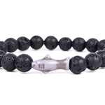 A beaded stretch Fahlo bracelet made of black porous lava stones with a central shark  charm, shown on a plain white background. Available at Be Charmed