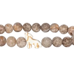 A beaded stretch Fahlo bracelet made of round, mottled brown and beige stone beads, featuring a small white carved wolf charm in the center, shown on a plain white background. Available at Be Charmed