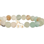 A beaded stretch Fahlo bracelet featuring round, polished beads in soft pastel shades of sage green, cream, and light brown, with a small white wolf charm at the center, shown on a plain white background. Available at Be Charmed