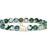 A beaded stretch Fahlo bracelet featuring round green and white marbled beads with a small white wolf charm outlined in gold, displayed on a clean white background. Available at Be Charmed