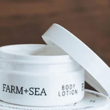White body lotion jar with 'Farm + Sea' branding on a wooden surface. Available at Be Charmed