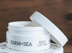 White body lotion jar with 'Farm + Sea' branding on a wooden surface. Available at Be Charmed