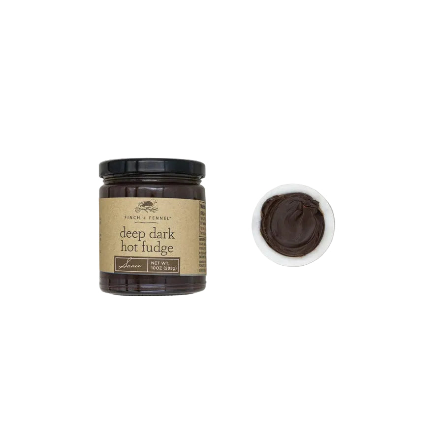 Jar of deep dark hot fudge with a small bowl of fudge on a light gray background. Available at Be Charmed