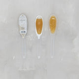 Two honey sticks with a label on a light gray background. Available at Be Charmed