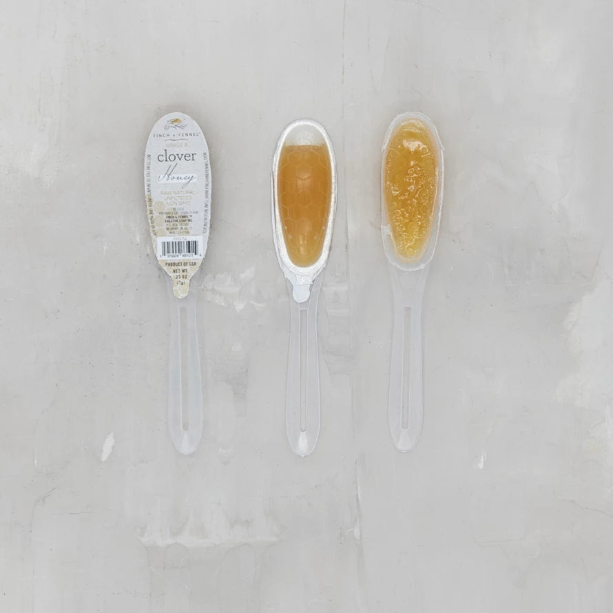 Two honey sticks with a label on a light gray background. Available at Be Charmed