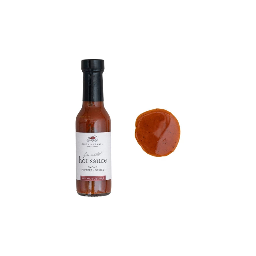 Bottle of hot sauce with a droplet of sauce on a white background. Available at Be Charmed