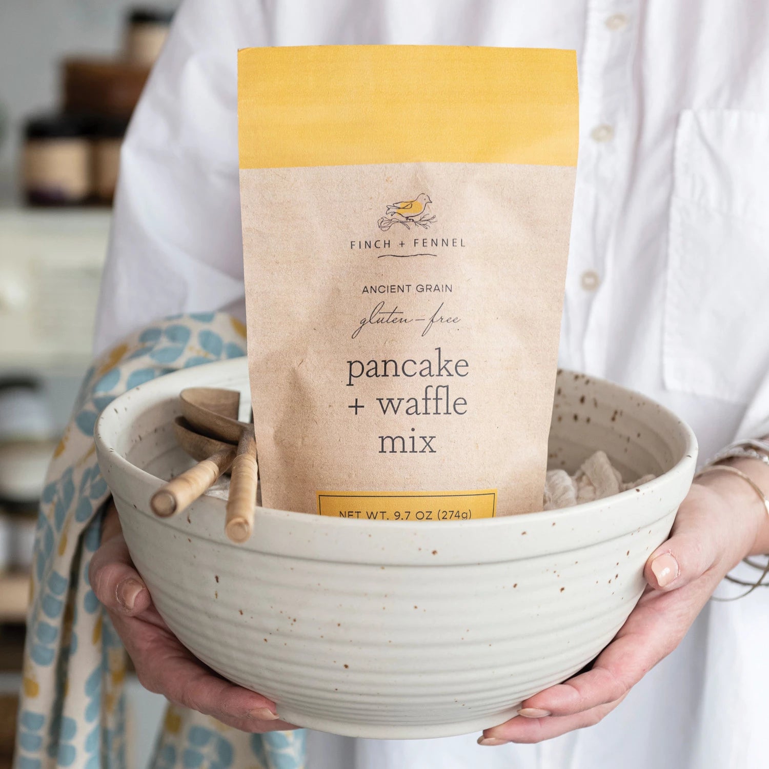 Person holding a bowl with a package of gluten-free pancake and waffle mix. Available at Be Charmed