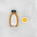Bottle of mesquite honey with a close-up of honey on a white background. Available at Be Charmed