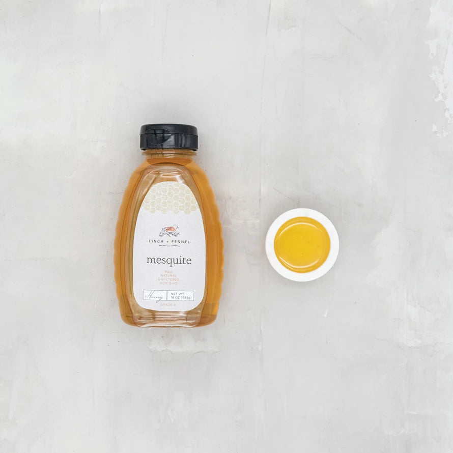 Bottle of mesquite honey with a close-up of honey on a white background. Available at Be Charmed