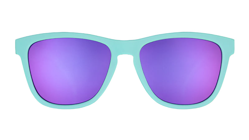 Front view of a pair of tGoodr teal blue sunglasses with purple polarized lenses, featuring the brand name 'Goodr' on the side. Available at Be Charmed